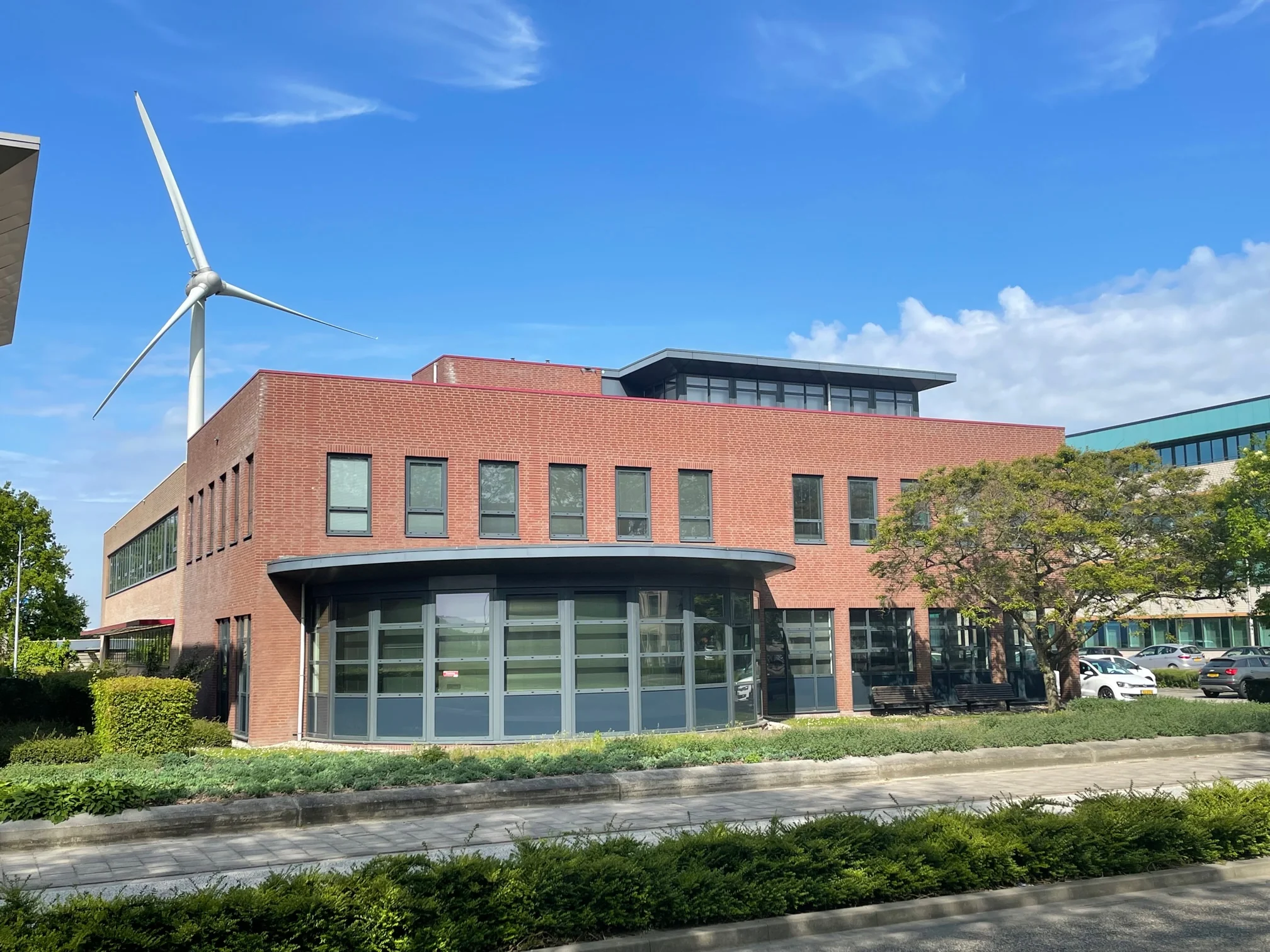 Modern rood bakstenen kantoorgebouw aan de Rivium 4e Straat met een windturbine op de achtergrond.